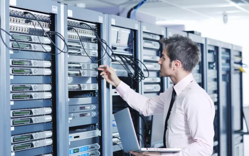 Man holding laptop in front of server containers